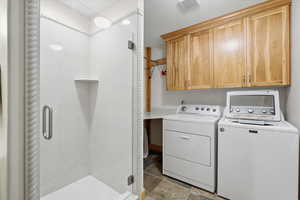 Laundry area featuring washer and dryer, light stone finish floors, and cabinet space