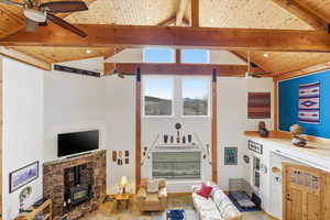 Living room featuring ceiling fan, a wood stove, plenty of natural light, and a high wood beamed ceiling