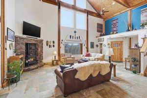 Living area with a wood stove, ceiling fan, a vaulted wood ceiling, and stone finish flooring