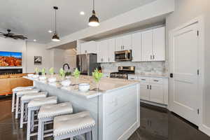 Kitchen with white cabinets, pendant lighting, stainless steel appliances, a center island with sink, and open floor plan