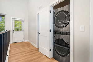 Laundry area featuring light wood-style flooring, stacked washer and dryer, a chandelier, and a high ceiling