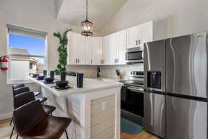 Kitchen featuring stainless steel appliances, lofted ceiling, light stone countertops, white cabinets, and light wood-style floors