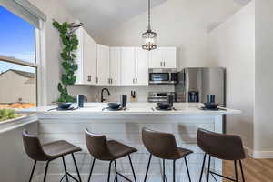 Kitchen featuring lofted ceiling, a kitchen breakfast bar, white cabinets, a peninsula, and stainless steel appliances