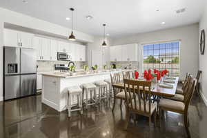 Kitchen featuring white cabinetry, stainless steel appliances, granite floors, a kitchen breakfast bar, and a center island with sink