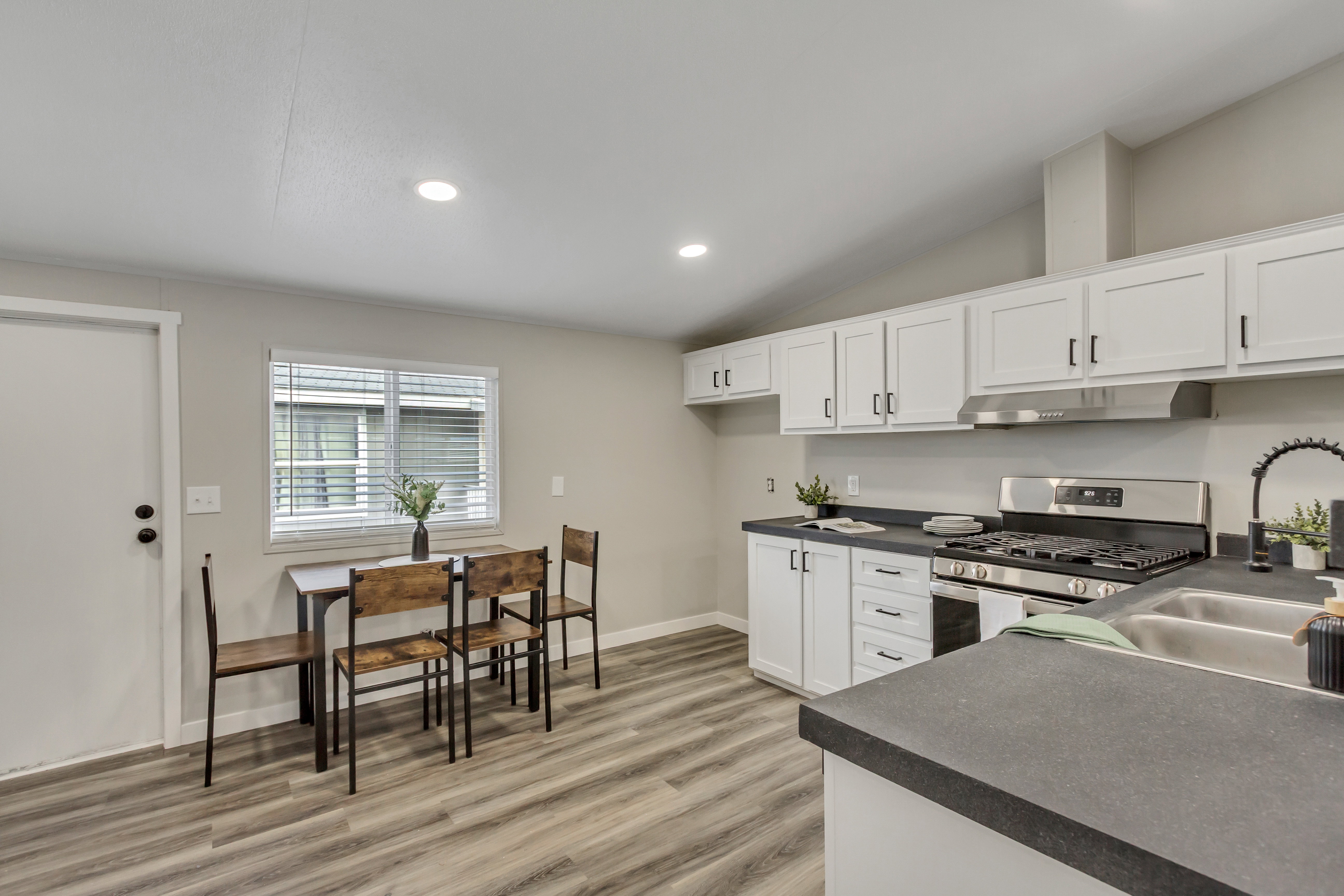 Kitchen featuring dark countertops, white cabinetry, vaulted ceiling, stainless steel gas range, and light wood-style floors