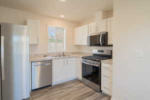 Kitchen featuring stainless steel appliances, white cabinetry, light countertops, light wood-style flooring, and recessed lighting