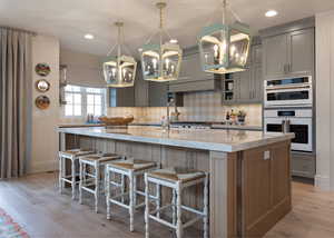 Kitchen featuring light stone countertops, a kitchen bar, a kitchen island with sink, white double oven, and light wood-style flooring
