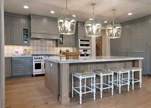 Kitchen with light stone counters, range with two ovens, a breakfast bar area, a large island with sink, and double oven