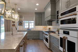 Kitchen featuring white appliances, gray cabinets, light stone counters, light wood-style flooring, and an island with sink
