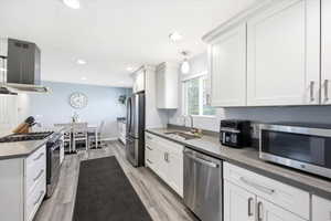 Kitchen featuring stainless steel appliances, island range hood, white cabinetry, light wood-type flooring, and recessed lighting