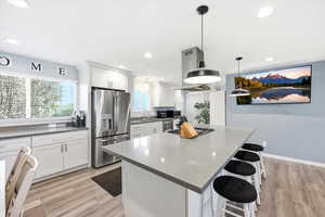 Kitchen with a breakfast bar, white cabinetry, light wood-type flooring, and stainless steel appliances