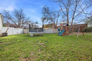 Fenced backyard featuring a trampoline and a playground