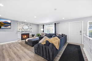 Living room with light wood-style flooring, a stone fireplace, and recessed lighting