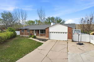 Single story home with covered porch, driveway, brick siding, a chimney, and a garage