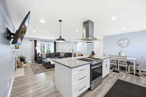 Kitchen with stainless steel range with gas stovetop, open floor plan, a center island, island range hood, and light wood finished floors