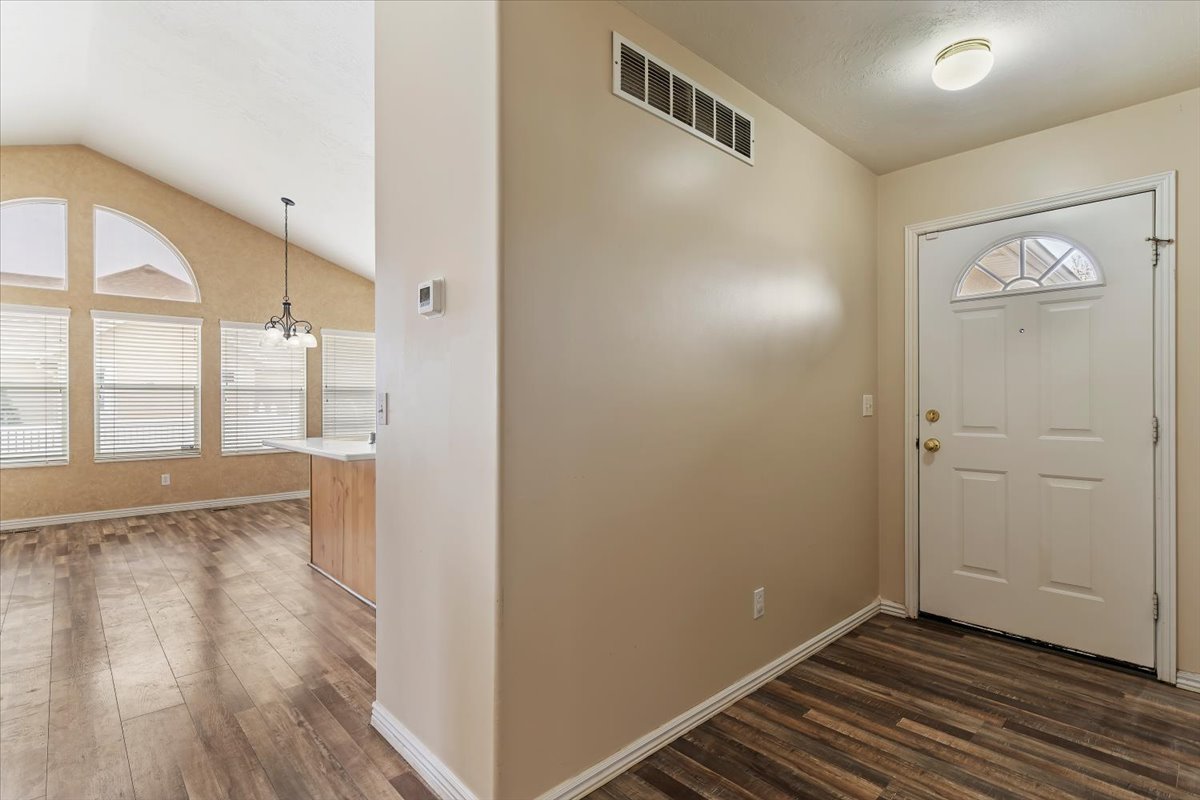 Foyer entrance featuring dark wood-type flooring, vaulted ceiling, and hanging lights