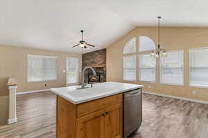Kitchen featuring a stone fireplace, light countertops, dishwasher, a ceiling fan, and open floor plan