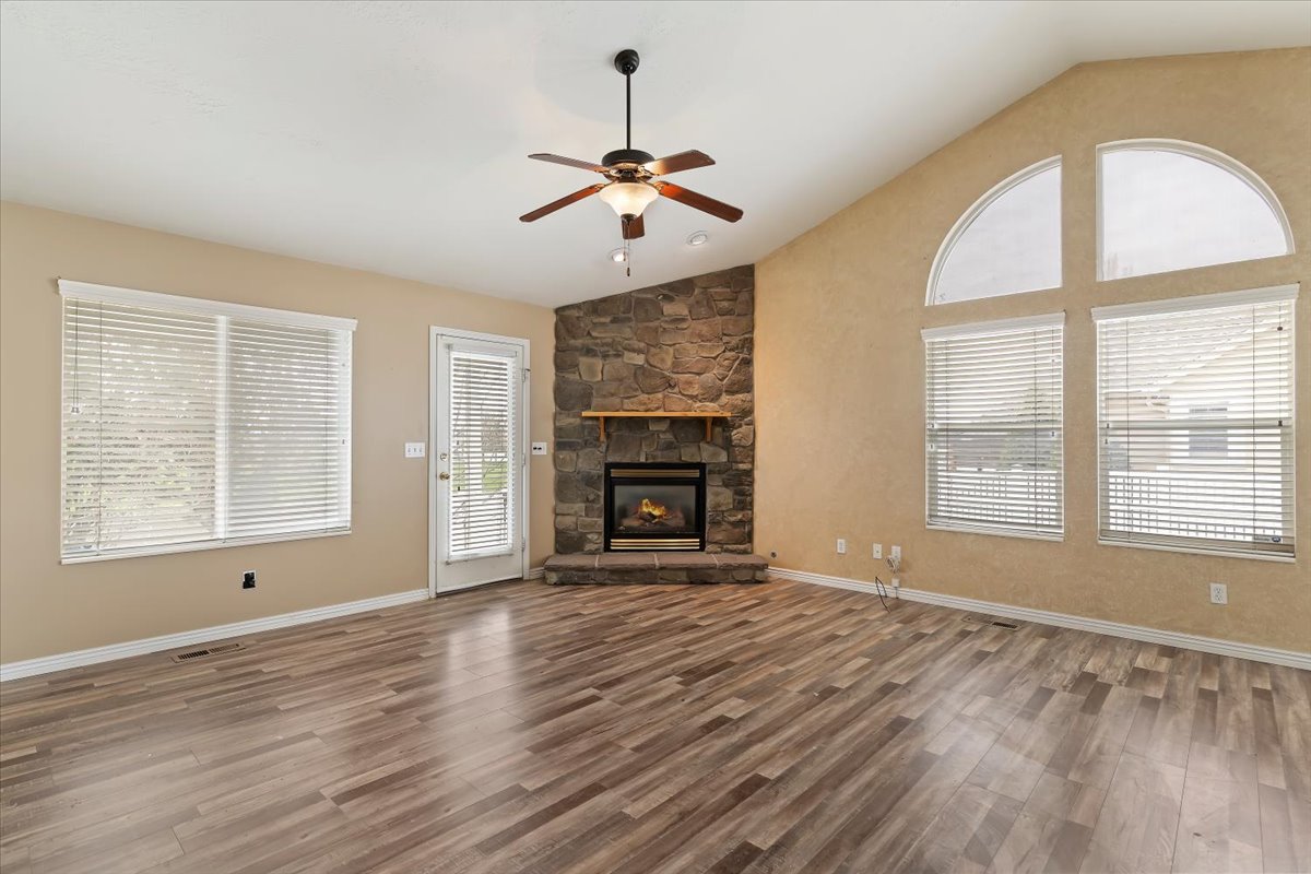 Unfurnished living room featuring ceiling fan, lofted ceiling, dark wood-type flooring, and a stone fireplace