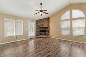 Unfurnished living room featuring ceiling fan, lofted ceiling, dark wood-type flooring, and a stone fireplace