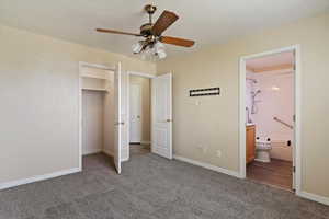 Unfurnished bedroom featuring a spacious closet, dark colored carpet, a ceiling fan, and connected bathroom