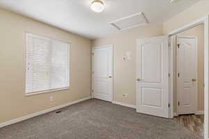 Unfurnished bedroom featuring attic access and dark carpet