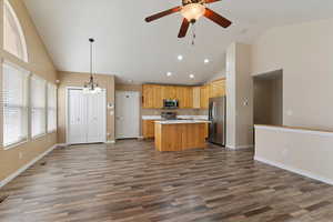 Kitchen featuring open floor plan, vaulted ceiling, light countertops, a kitchen island with sink, and a ceiling fan