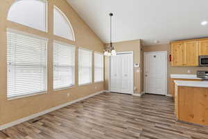 Kitchen with light countertops, suspended lighting, light wood finish cabinets, stainless steel appliances, and dark wood-style floors