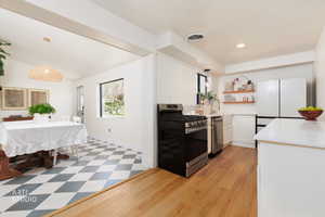 Kitchen with stainless steel appliances, plenty of natural light, white cabinets, open shelves, and lofted ceiling