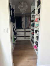 Walk in closet with light wood finished floors and hanging lights