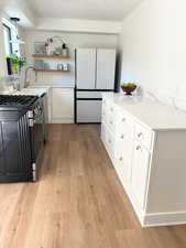 Kitchen featuring white cabinets, stainless steel range with gas stovetop, freestanding refrigerator, light wood finished floors, and a textured ceiling