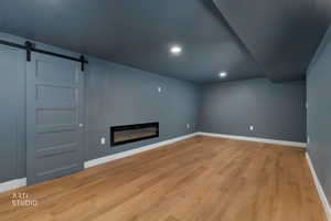 Unfurnished living room featuring a barn door, light wood-type flooring, a glass covered fireplace, and recessed lighting