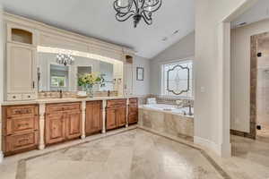 Primary Suite Bathroom with suspended lighting, inlaid floor details, double vanity, a bath, and vaulted ceiling