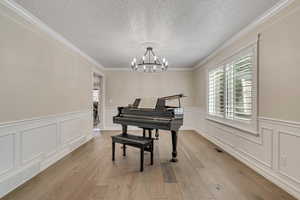 Sitting room with ornamental molding, a textured ceiling, a wainscoted wall, a chandelier, and healthy amount of natural light