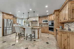 Kitchen featuring a kitchen breakfast bar, light stone counters, stainless steel appliances, a center island, and pendant lighting