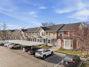 View of front of house featuring covered and uncovered parking, brick siding, a residential view, roof with shingles, and a balcony