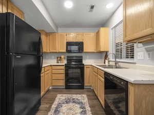 Kitchen featuring black appliances, light wood finish cabinets, light countertops, a textured ceiling, and dark wood-style flooring