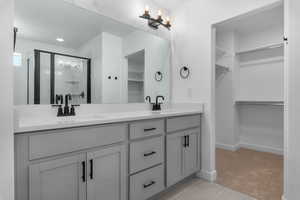 Full bathroom featuring double vanity, light tile patterned floors, a spacious closet, and a shower stall