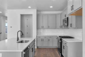 Kitchen with stainless steel appliances, dark wood-style floors, gray cabinetry, a center island with sink, and light stone countertops