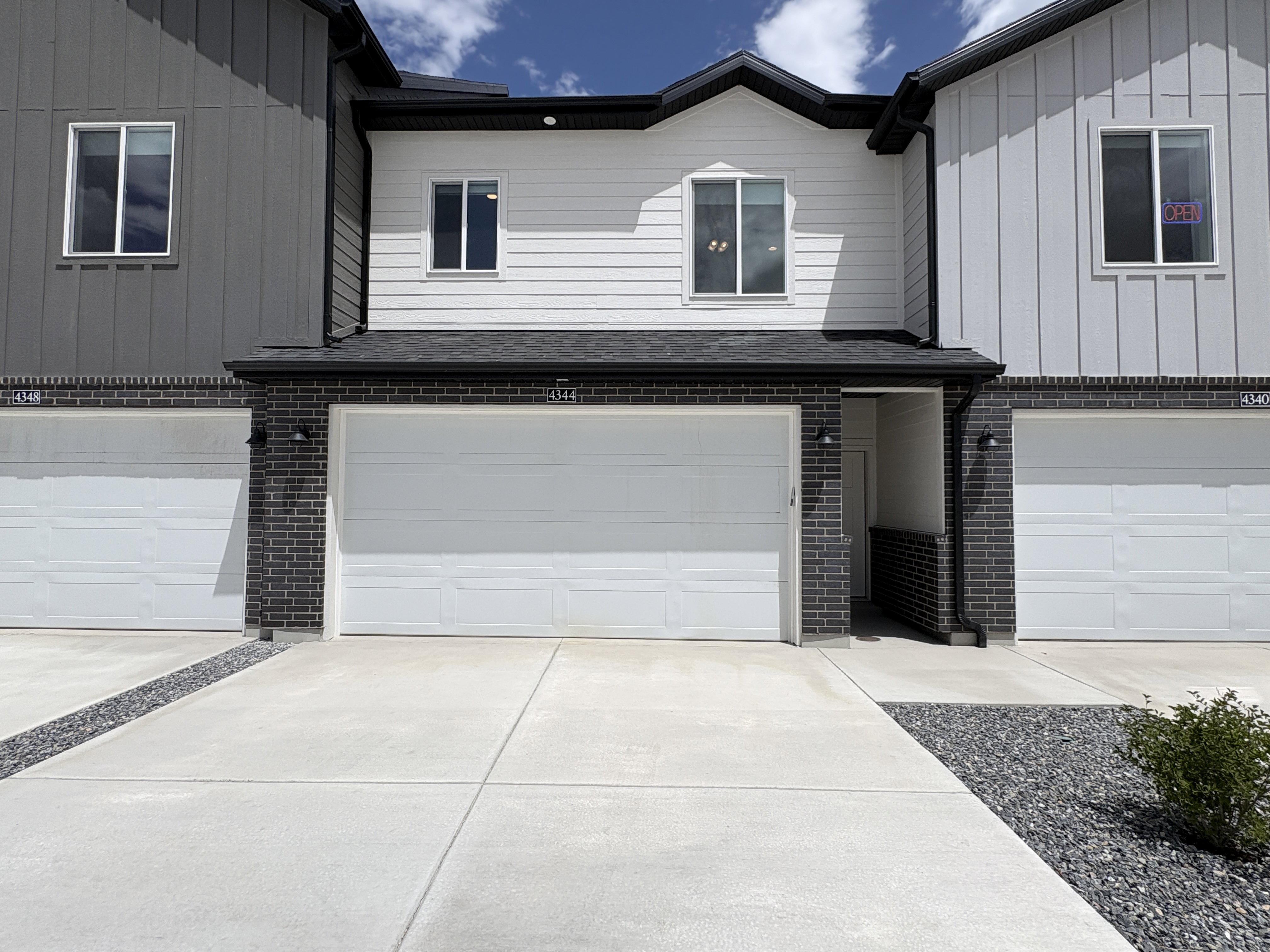 Modern townhome exterior featuring white horizontal siding, dark vertical siding, and dark brick accents