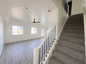Stairs with a textured ceiling, wood finished floors, and ceiling fan