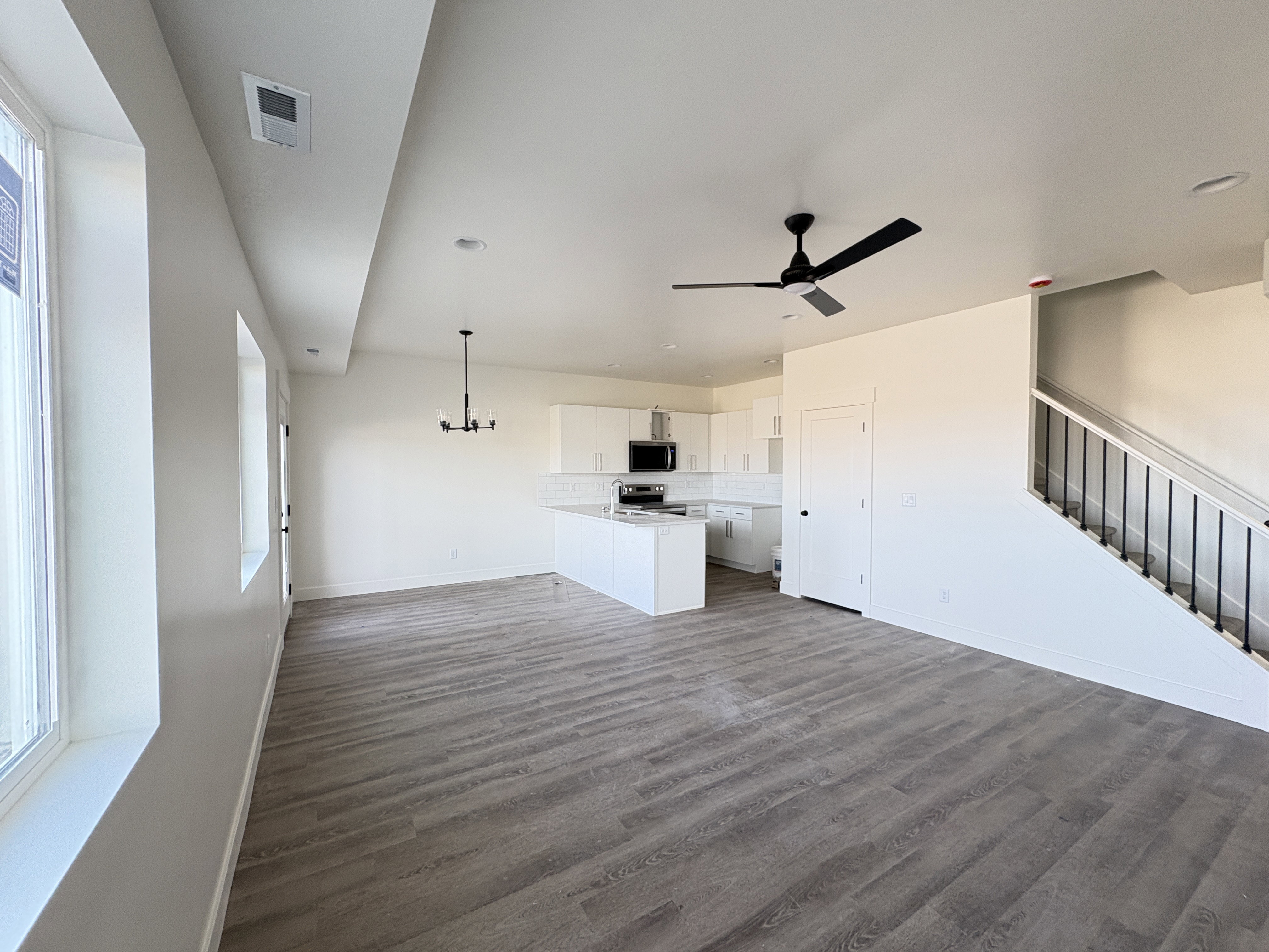 Unfurnished living room featuring dark wood-style flooring, a ceiling fan, and suspended lighting
