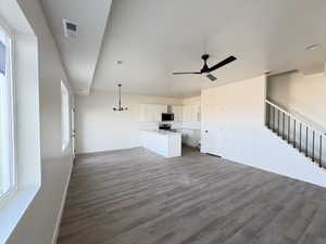 Unfurnished living room featuring dark wood-style flooring, a ceiling fan, and suspended lighting
