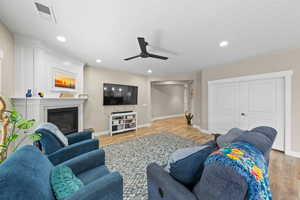 Living room featuring light wood-type flooring, a ceiling fan, a glass covered fireplace, and recessed lighting