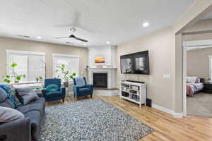 Living area with ceiling fan, light wood-type flooring, a fireplace, recessed lighting, and a textured ceiling