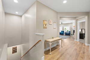 Corridor with light wood finished floors, recessed lighting, and an upstairs landing