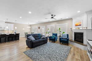 Living room with light wood-style flooring, a ceiling fan, a textured ceiling, a glass covered fireplace, and recessed lighting