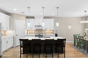 Kitchen featuring an island with sink, a breakfast bar area, light wood-style floors, hanging light fixtures, and two tone cabinets