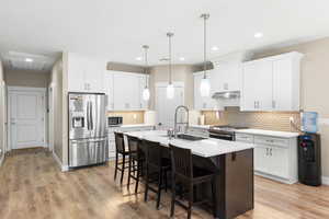 Dual tone kitchen featuring a kitchen breakfast bar, stainless steel appliances, an island with sink, hanging light fixtures, and two tone cabinetry