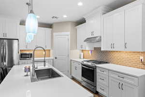 Kitchen featuring white cabinets, stainless steel appliances, hanging light fixtures, and light stone countertops
