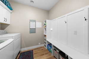Laundry area with light wood-style flooring, washer and dryer, cabinet space, and electric panel